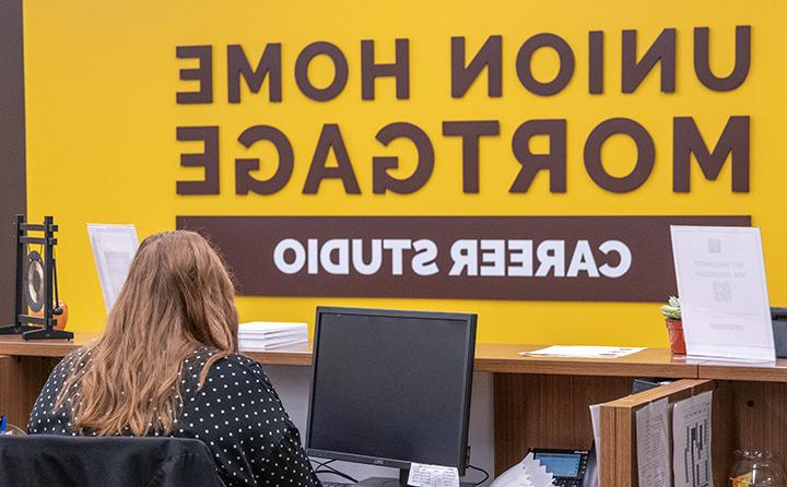 BW Career Studio Sign with Woman Sitting in Front of Computer